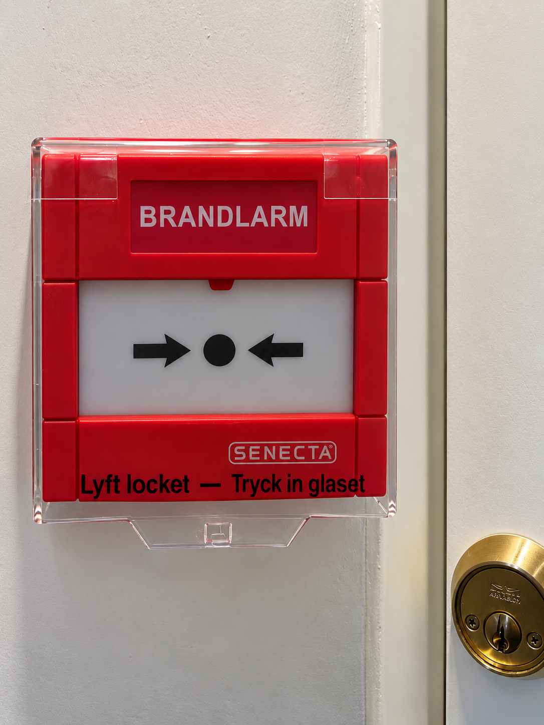 Senectas manuella brandlarmsknapp med skyddslock monterad på vägg